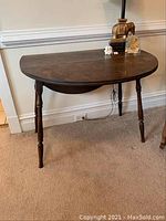Full view of half-moon shaped wooden drop leaf table standing on carpeted floor against wall.