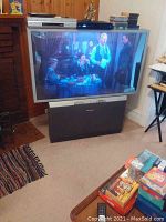 Front view of large Panasonic TV with screen showing a scene, Sony DVD/VHS system on top with stacked tapes