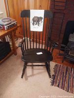 Front view of black wooden rocking chair with bear and moose towel on backrest, next to a fireplace.