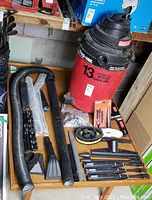 Full view of Shop-Vac and accessories including hoses, nozzles, extension tubes, brush attachments, and small accessory parts shown on wooden surface.