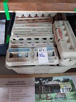 Several egg carton trays holding approximately a dozen golf balls each, stacked, stored in a garage setting with visible wear on balls.