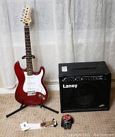 Full overview of red electric guitar on stand next to Laney amp with footswitch and strap on floor