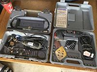 Two open plastic carrying cases showing Dremel power tools and multiple attachments inside on a work surface.