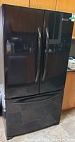 Front view of closed black French door refrigerator with bottom freezer drawer
