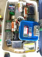 Open plastic tote filled with various small containers of screws, nails, washers, nuts, and bolts, showing brand packaging and assortment of hardware items.