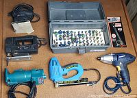 Grouped shot of seven items including Makita trimmer, Black & Decker jig saw, Mastercraft impact driver, Jobmate sander, arrow nailer, toolbox with router bits, and vintage wrench
