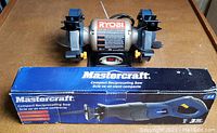 Photo showing the Mastercraft reciprocating saw box and Ryobi bench grinder side by side on a wooden table.