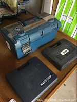 Blue Rubbermaid toolbox, black Mastercraft case, and black Paslode case on a table surface