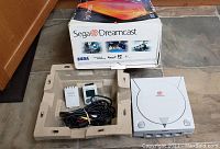 Console, original box, molded tray, power brick, VMU and A/V cable arranged on floor.