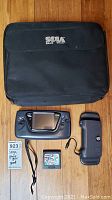 Full lot shown on wooden floor: Sega Game Gear console, Sonic the Hedgehog 2 game cartridge, Powerback accessory, and black Sega carrying case with zipper.