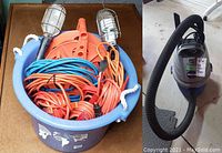 Full view of blue tub with assorted extension cords, cord wrap holders, and two shop lights, alongside Shop Vac unit with hose attached