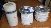 Overall view: two spools of white electrical wire and one roll of Polytarp plastic sheeting on table