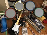 Overview of drum kit with colored rims, guitar controller, Beatles game, silencer pack, drumsticks, microphone and stand box