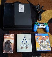 Overview of PS4 console, power cord, controller, Prototype figure, Assassin’s Creed Unity and Apex Legends games