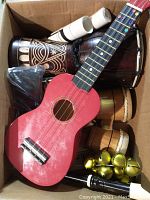 Top view of the box showing red ukulele on top, wooden bongos, white recorders, and golden jingle bells inside the box.