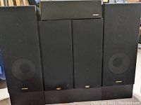 Front view of all five speakers showing two large Fisher speakers, one Energy center speaker on top, and two Maximum Audio Gold speakers with black grill covers.