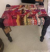 Side angle photo showing the black turned wooden legs and colorful woven fabric seat of the bench.