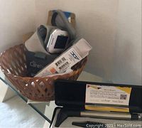 Three health aid medical devices shown including a blood pressure monitor in original box inside a brown woven basket, and a black otoscope case open showing accessories.