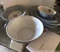 Photo showing a large handled bowl, two smaller floral bowls, and additional platters stacked showing their shape and designs.