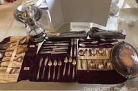 Wide-angle view of assortment of silver-plated flatware and utensils laid out on velvet-lined cases and a silver tray.
