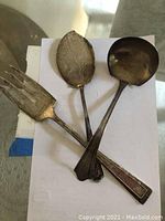 Three-piece sterling silver serving ware including a fork, serving spoon, and ladle, arranged on white paper.