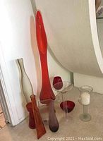 Several photos of midcentury glassware assortment placed on floor near corner wall. Includes several slender vases in orange-red, frosted white, ambers and purple tones, red small vases and bowls, clear glass cocktail glass and candle holder with a white candle.
