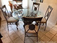 Front view of round glass top table with 4 upholstered metal-frame chairs around it on tiled floor.