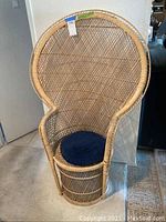 Full front view of wicker peacock chair showing back arch, base and round blue cushion