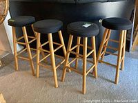 Four wooden bar stools with black round upholstered seats arranged on carpet.