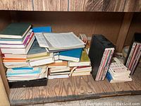 Multiple stacks of assorted religious books and magazines on a wooden shelf, various sizes and colors visible.