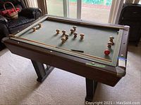 Full view of bumper pool table showing felt surface with bumper pins and a single red ball.