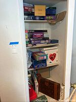 Shelf full of various boxed board games and puzzles including Balderdash, Taboo, Trivid, Scrabble, and others seen stacked in closet shelving