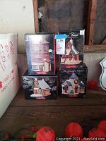 Four boxed porcelain collectible buildings from the Our Town series arranged on a wooden surface.