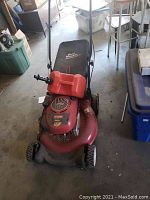 Front view of red Craftsman lawn mower with a black Dust Blocker grass catcher bag and a red gas can attached to the handle.