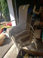 Four beige outdoor patio chairs stacked inside a garage with mesh fabric and metal frames.