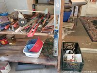 Wide view of the assortment of hand tools including saws, screwdrivers, level, tape measure, brushes, and extension cords placed on a wooden surface, showing condition and quantity.