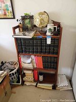 Full view of wood bookshelf containing books, a globe, framed art piece, animal figurines and other items around the unit.
