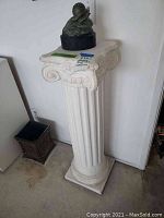 Full view of white classical column pedestal with bronze sculpture and metal wastebasket on floor nearby