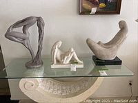 View of all 3 female statuettes displayed on a glass table.