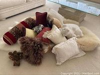 Display of decorative pillows, sheepskins, and part of the stuffed animals on a carpeted floor near a glass-top table and couch.