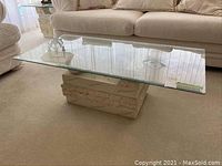Full view of coffee table from side, with glass top and faux marble base, placed on carpet in a living room.