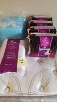 Photo showing one bundle of blue disposable bed protection pads and four purple and black packages of Poise Overnight Pads on a mattress.