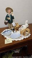 View of Byers' Choice Carolers figure, three bunny figurines, two porcelain dishes on a crocheted doily