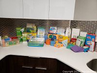 Wide view of cleaning supplies displayed on a kitchen counter showing mostly new products arranged in rows including Swiffer dusters, scrub pads, boxes of Scrub Daddy sponges, Magic Erasers, gloves, and cleaning clothes.