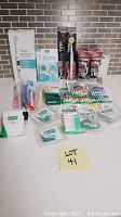 Lot of dental hygiene products arranged on white surface including Dr. Tung's Ionic Toothbrush, toothbrush heads covers, Proxabrushes, dental floss with brands Colgate, GUM, REACH