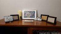 Wood cabinet top with floral mulberry paper art center, cream Luminara candle and remote left, and four picture frames right and front.