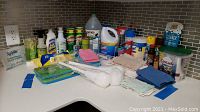 Photo of various household cleaning bottles, powders, wipes and folded cleaning rags on countertop in kitchen corner.