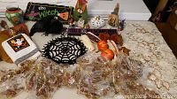 Wide view of assorted fall and Halloween decorations on a table including mirror, pumpkin decor, crow figurine, signs, spider web placemat, and beaded garlands wrapped in plastic.
