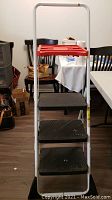 Front view of white metal 3-step ladder with red top shelf, black steps, labeled 'COSCO'