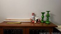 Full view of green lighted candle holder trio, assorted rolls of wrapping paper, ribbons, and other gift supplies displayed on wooden cabinet.